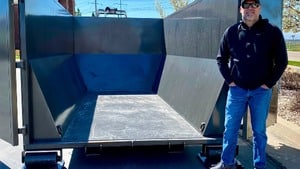 A man standing next to an empty 20 yard roll off dumpster.