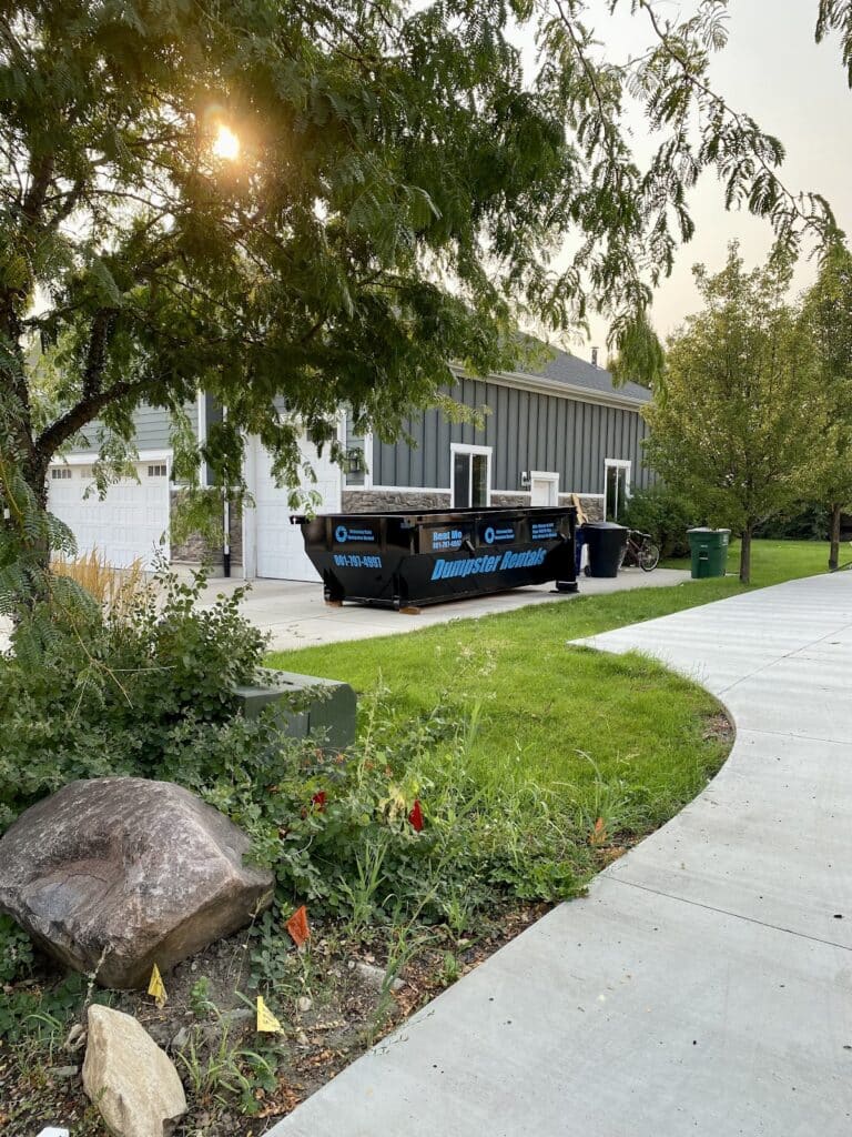 A large black dumpster for rent parked in a residential driveway.