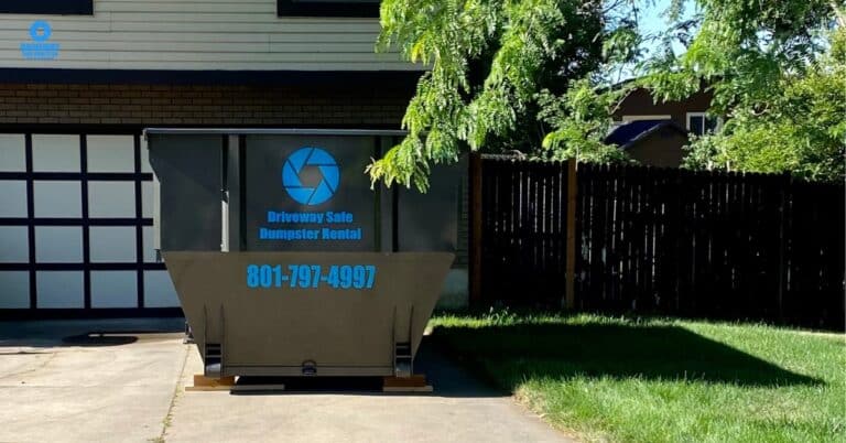 Person holding old electronics next to a dumpster