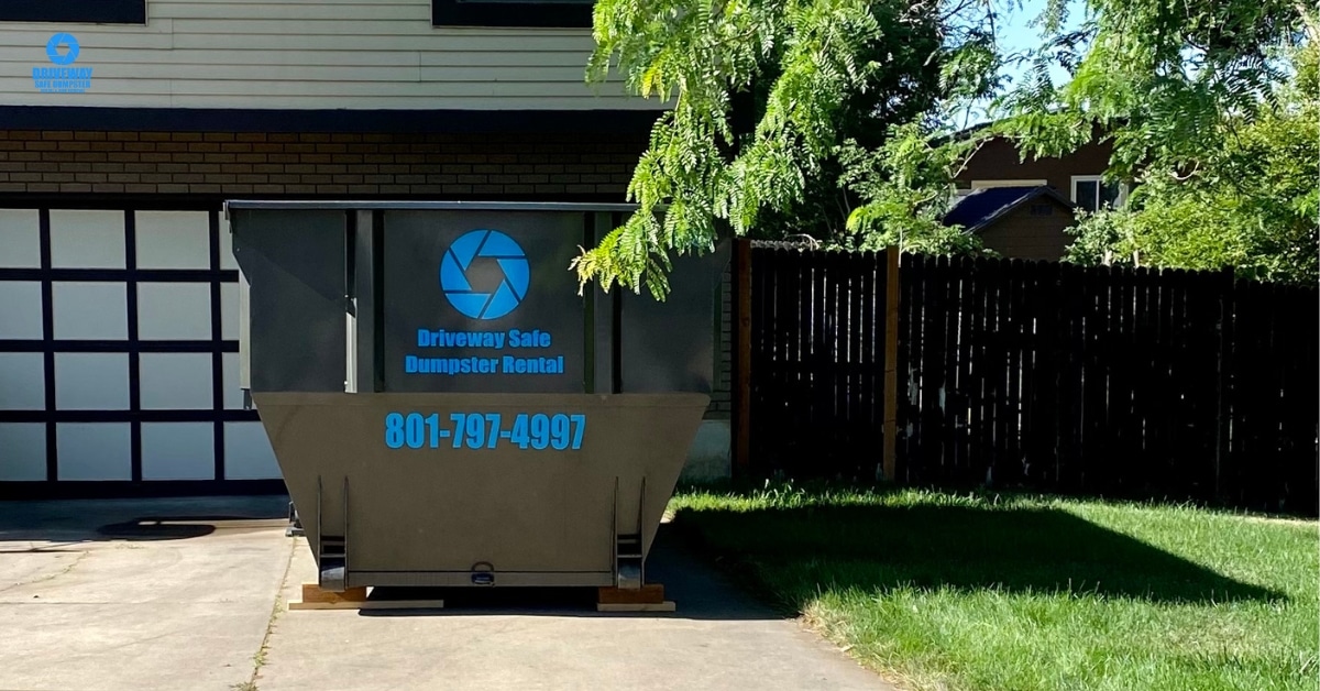 Person holding old electronics next to a dumpster