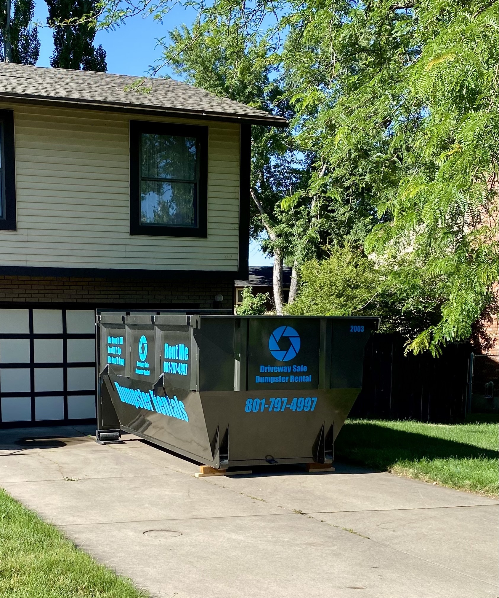 A 15 yard roll off dumpster parked in a residential driveway in front of a house.
